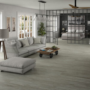 Salón abierto con suelo porcelánico efecto madera, sofá gris, mesa baja y mampara metálica