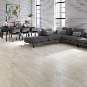 Salón con pavimento cerámico imitación madera claro, sofá gris y pared de ladrillo blanco