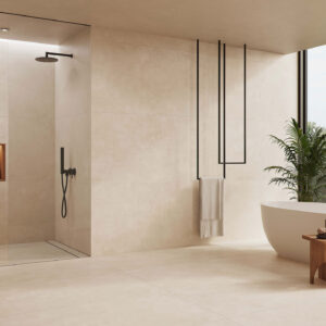 AMB-KTL_COLUMBIA-SAND_75x150-R_BAJA Exposición de baño con azulejos beige, ducha a la italiana negra, bañera exenta y planta