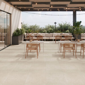 Terraza expositora con pavimento cerámico beige, mesas y sillas de madera y jardineras