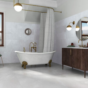 Baño expositor con bañera exenta de patas doradas, revestimientos cerámicos blancos y mueble lavabo.