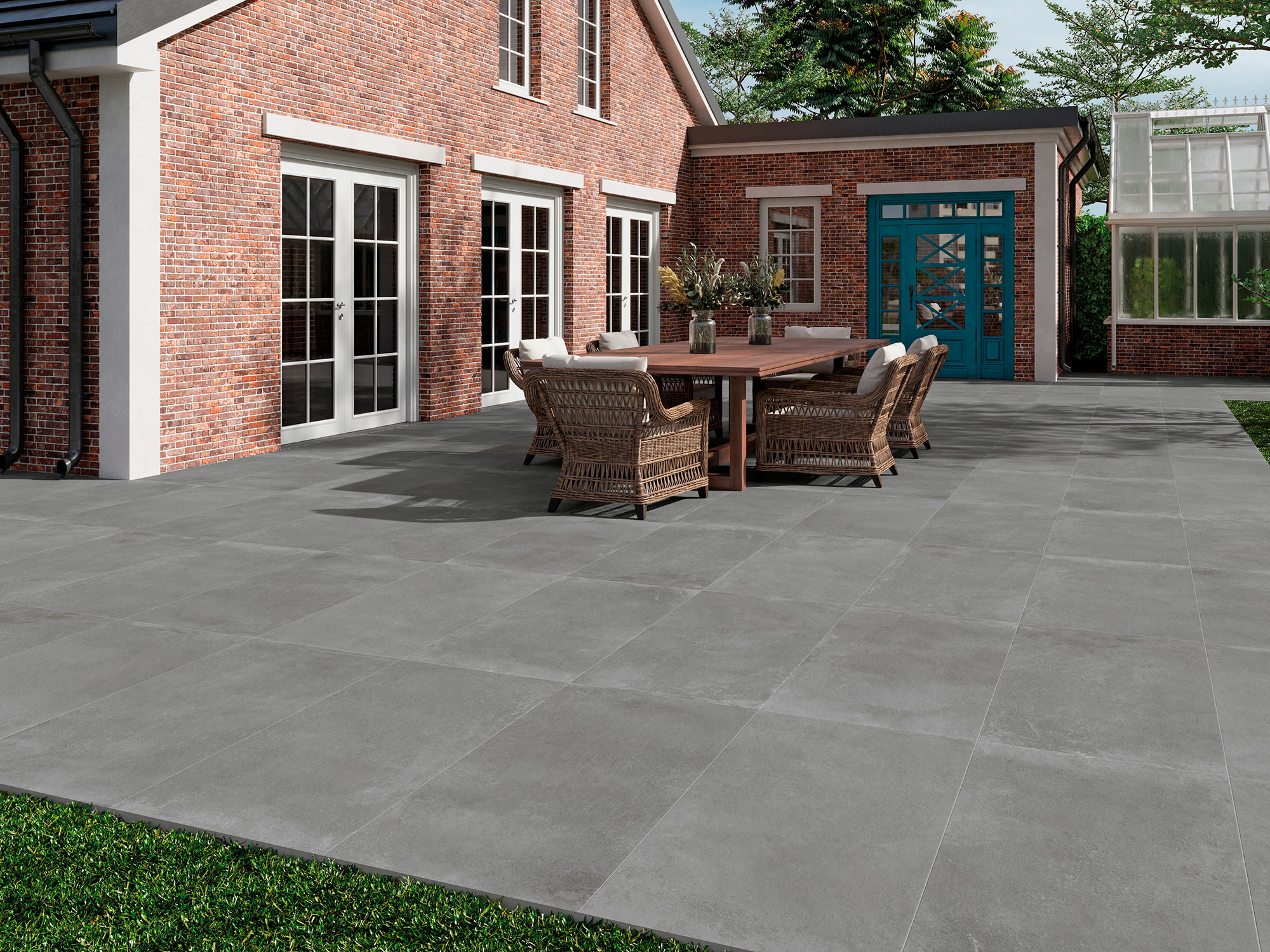 AMB-SONDER-ANTRACITE-60X120-20MM Terraza exterior con pavimento cerámico gris y zona de comedor junto a casa de ladrillo.