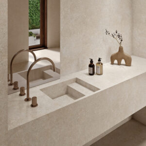 Lavabo integrado y encimera de gres beige con grifo bronce, dispensadores y jarrón