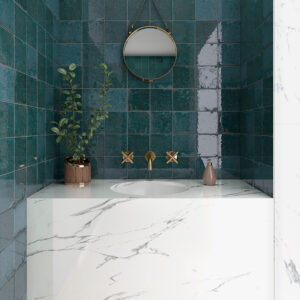 Lavabo empotrado con encimera efecto mármol, grifería dorada y azulejos cerámicos verde azulado.