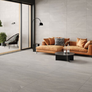 BELLEVUE-GREY-60X120_30X60 Showroom con pavimento y revestimiento cerámico gris, sofá mostaza y terraza.