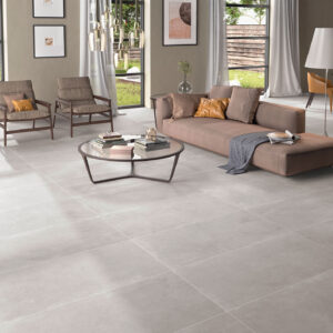 Salón luminoso con pavimento cerámico gris mate, sofá bajo, mesa de centro circular y ventanales.