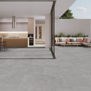 COLUMBIA-DARK-GREY-60x120-RGB-AMB-01 Interior y terraza abiertos con suelo cerámico gris continuo, cocina y sofá exterior.