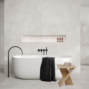 Bañera exenta en baño con pavimento y revestimiento cerámico en tonos claros.