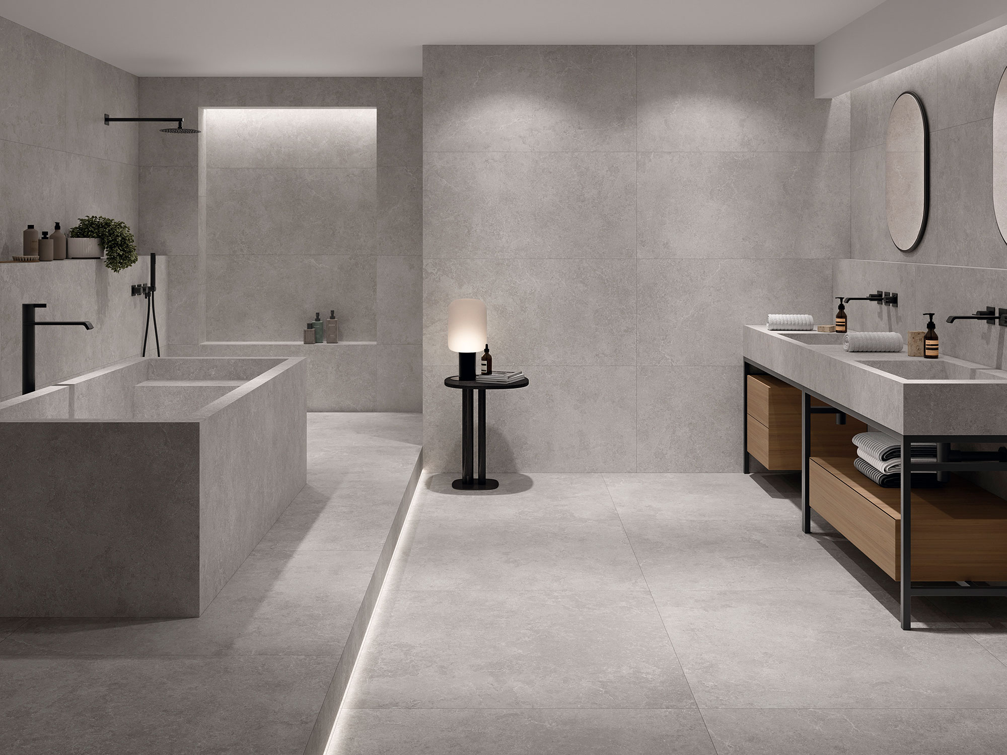 Baño expositor con grandes azulejos cerámicos grises, bañera integrada y doble lavabo.