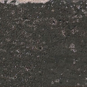 Azulejo cerámico oscuro texturizado con borde irregular y restos de mortero