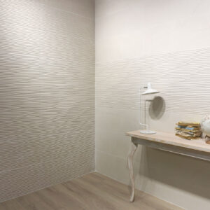 Rincón con azulejos cerámicos texturizados en ondas, consola de madera, lámpara y globo