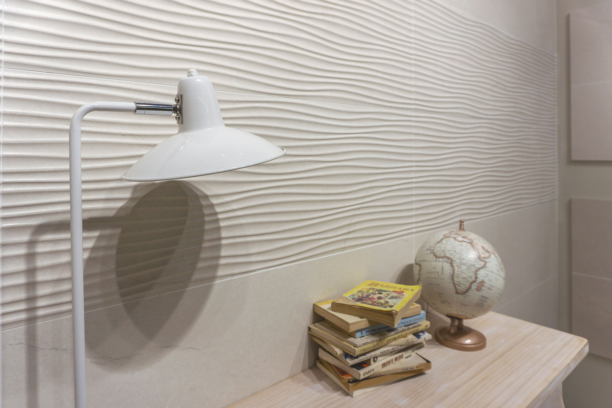 Detalle de revestimiento cerámico ondulado blanco con lámpara, libros y globo