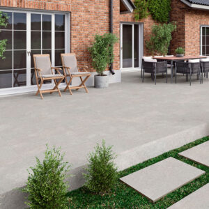 Terraza con pavimento cerámico gris, fachada de ladrillo, mobiliario exterior y losas en césped