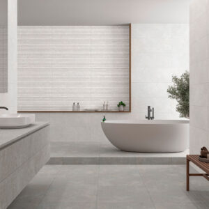 Baño expositivo con pavimento y revestimiento cerámico gris, bañera exenta y lavabo