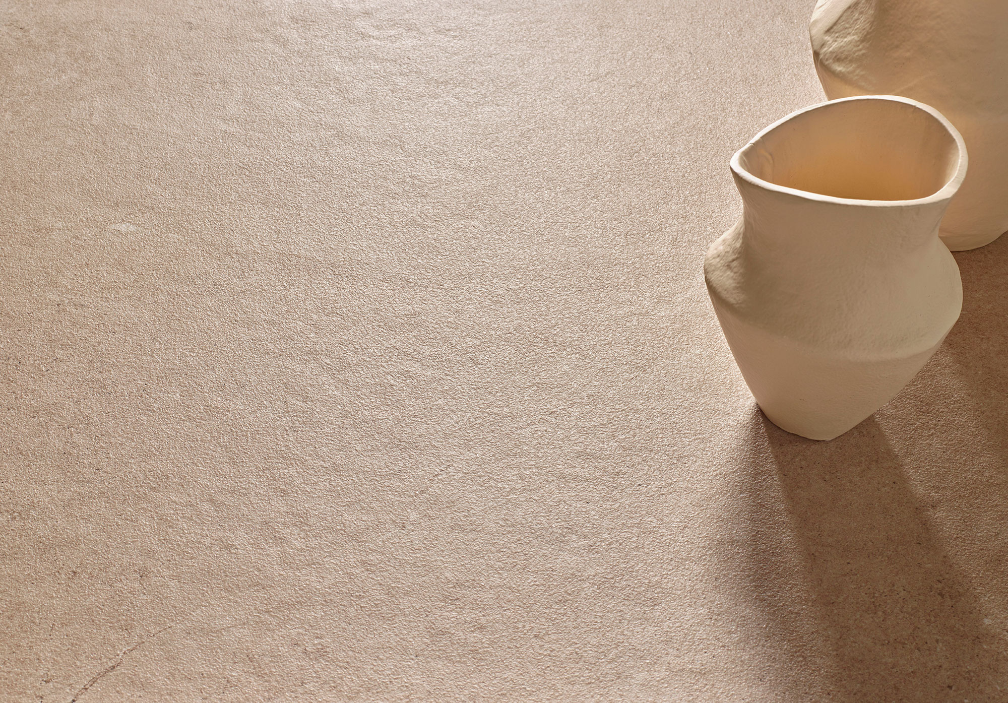 Suelo cerámico texturizado beige con jarrones escultóricos crema y sombra