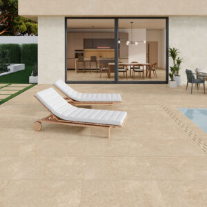Terraza junto a piscina con gres beige efecto piedra, tumbonas blancas y comedor exterior