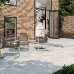 Terraza con pavimento cerámico gris, muro de ladrillo y sillas metálicas