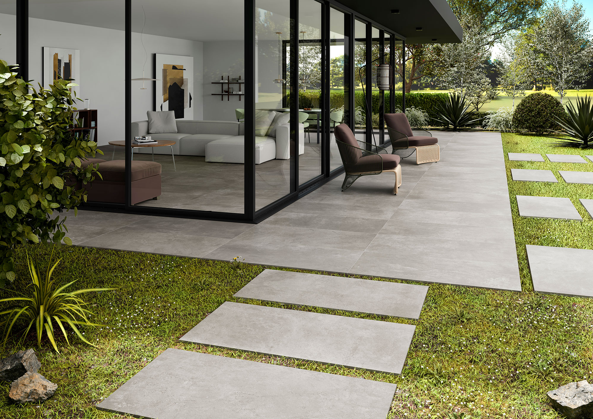 Terraza con grandes losas cerámicas grises, camino en placas sobre césped y salón acristalado.