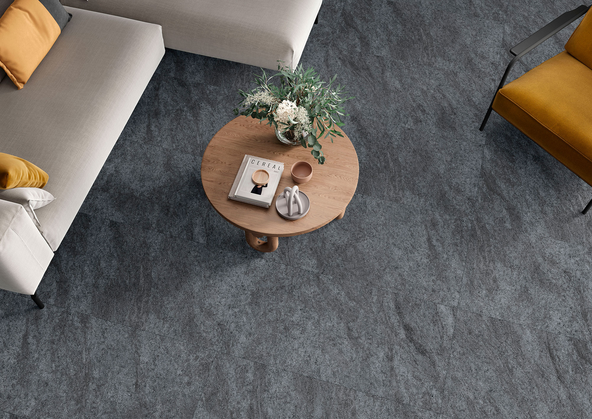 Salón desde arriba con pavimento cerámico gris texturado, mesa circular de madera y sofás