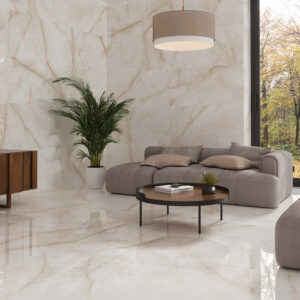STN-AMB-BALTRA-IVORY_120X120_120X60 Salón moderno con azulejos cerámicos efecto mármol crema, sofá, mesa y ventanal al bosque.