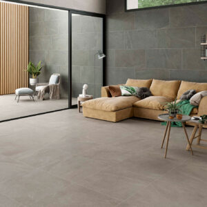 STN-AMB-BELLEVUE-INOUT-GRAPHITE-GREY-60X120+GREY-75X75 Salón con pavimento y revestimiento cerámico gris efecto piedra, sofá beige y terraza ajardinada