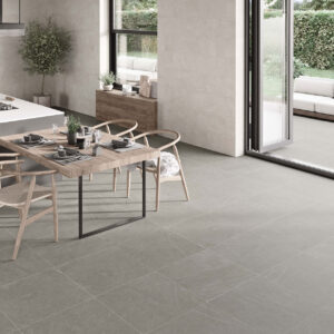 STN-AMB-BELLEVUE-INOUT-GREY-60X60_-IVORY-30X60-(SIMULADO) Cocina abierta con suelo cerámico gris, revestimiento mural, isla y comedor junto al jardín