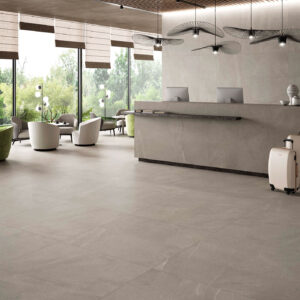 STN-AMB-BELLUEVE-GREY-120X120 Recepción de tienda: grandes azulejos grises, mostrador moderno y lounge junto a ventanales.