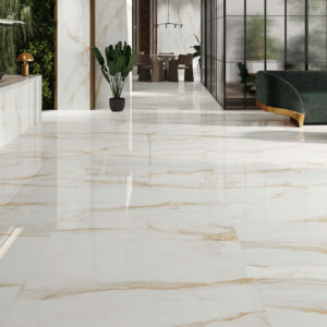 STN-AMB-CAMILE-GOLD-PULIDO-60X120 Showroom con suelo porcelánico blanco veteado dorado, mostrador, sofá verde y plantas