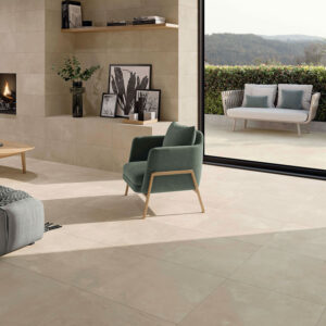 STN-AMB-ELEMENTI-BEIGE-60X60_30X60-INOUT-SALON Muestra de pavimento y revestimiento cerámico beige en salón con chimenea y terraza