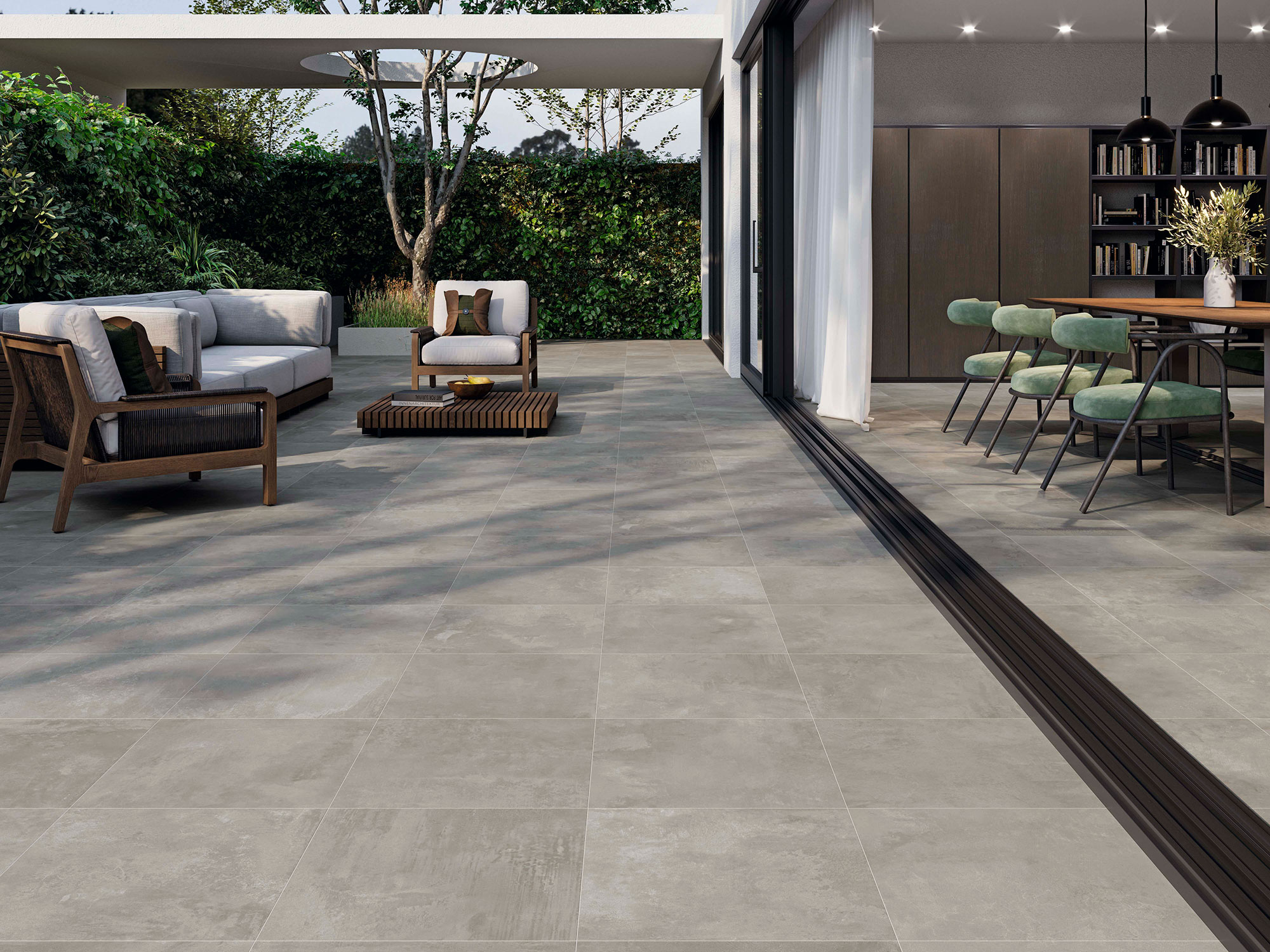 STN-AMB-ELEMENTI-GREY-45X45-INOUT Terraza y comedor abiertos con pavimento cerámico gris, sofás, mesa y jardín.