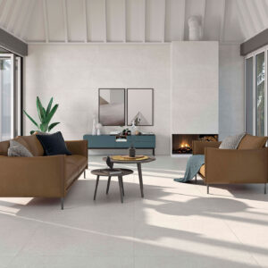 STN-AMB-HOMESTONE-ARGENT-100x100+PEARL-60x120 Sala moderna con suelos y paredes cerámicos claros, sofás marrón y chimenea.