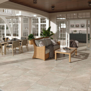 STN-AMB-ICARIA-BEIGE-60X60X2 Terraza de exposición con pavimento cerámico efecto piedra, muebles de rattan y plantas