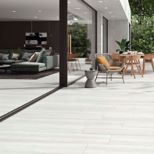 Terraza con pavimento cerámico efecto madera claro, mobiliario exterior y salón acristalado