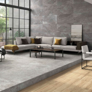 Sala de exposición con pavimento cerámico gris, paredes a juego, sofá seccional y ventanales