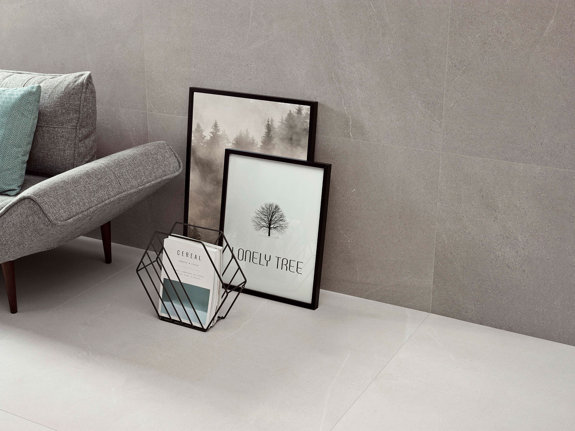 STN-DETALLE-BELLEVUE-GREY-WHITE-60X120 Rincón minimalista con pavimento y revestimiento cerámicos gris, sofá y marcos apoyados.