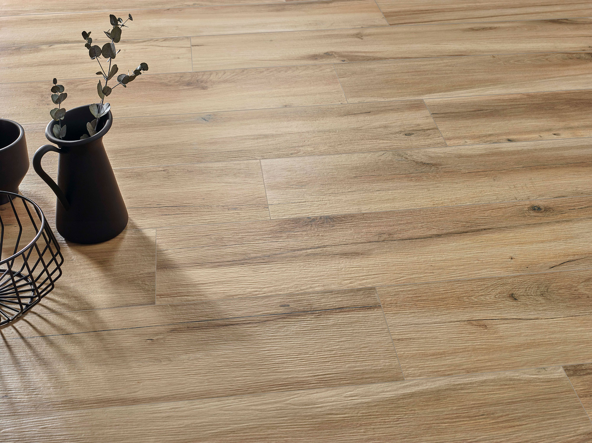 Suelo cerámico efecto madera roble claro en lama, con jarra negra y cesta decorativa