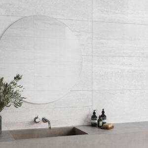 Baño minimalista con azulejos gris claro, espejo circular, lavabo, grifería y accesorios