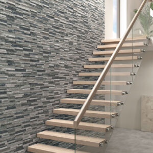 Escalera flotante de madera y vidrio junto a muro de revestimiento cerámico gris