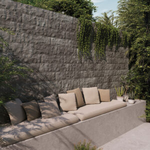 Banqueta exterior con cojines beige ante revestimiento cerámico texturado y plantas colgantes