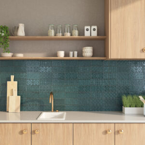 Cocina con salpicadero de azulejos cerámicos verdes estampados, encimera blanca y grifería dorada