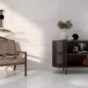 Salón minimalista con azulejos blancos grandes, butaca de madera, mueble y planta.