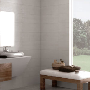 Baño exhibición con azulejos grises rectangulares, lavabo flotante y banco de madera junto a ventana