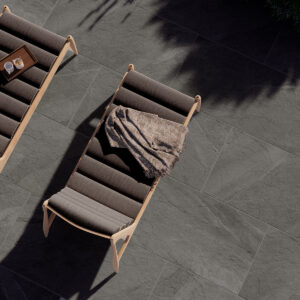 Dos tumbonas de madera y tela sobre pavimento cerámico gris con sombras y plantas