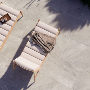 Tumbonas sobre pavimento cerámico gris efecto piedra, bandeja con tazas y manta