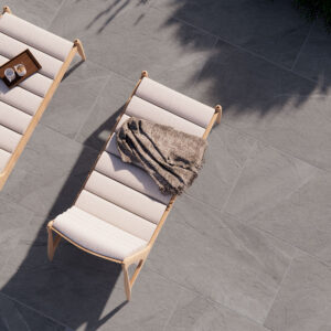 Dos tumbonas con cojines sobre pavimento cerámico gris efecto piedra, manta y bandeja