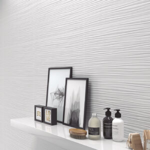 Pared cerámica blanca con relieve ondulado; estante muestra cuadros, botes, cepillo y jabones.