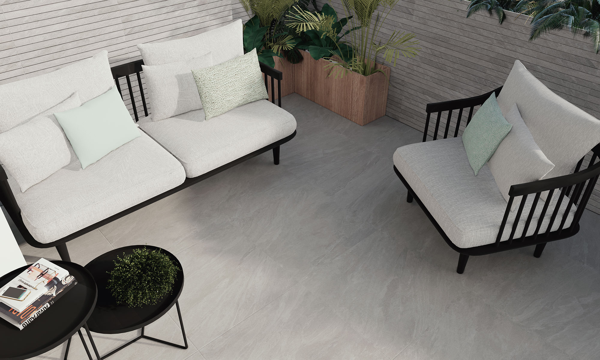 Terraza con pavimento cerámico gris efecto piedra, sofás claros y mesas negras