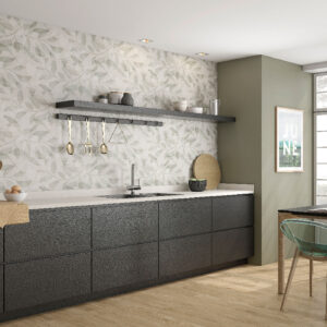 Cocina expositora con revestimiento cerámico de hoja, encimera clara y muebles oscuros.