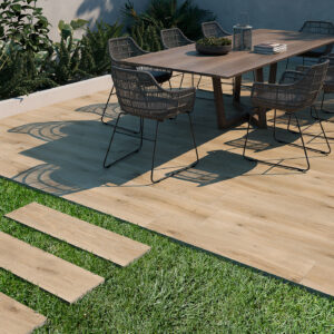Terraza con mesa y sillas sobre pavimento cerámico efecto madera y losas integradas en césped