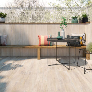 Terraza showroom con suelo cerámico efecto madera, banco, mesa redonda y cojines.